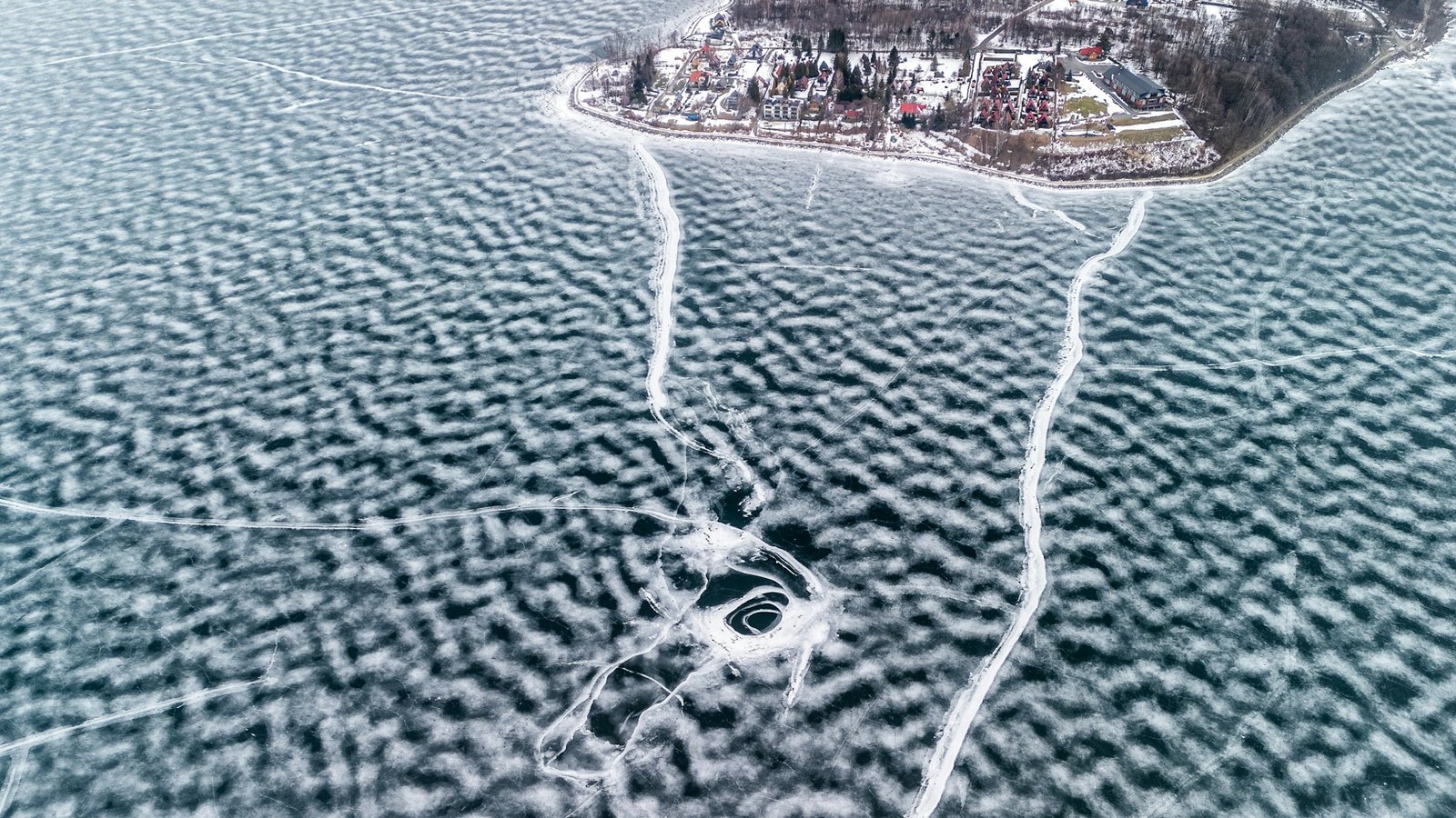 Aerial of a small lakeside community along a frozen northern shoreline.