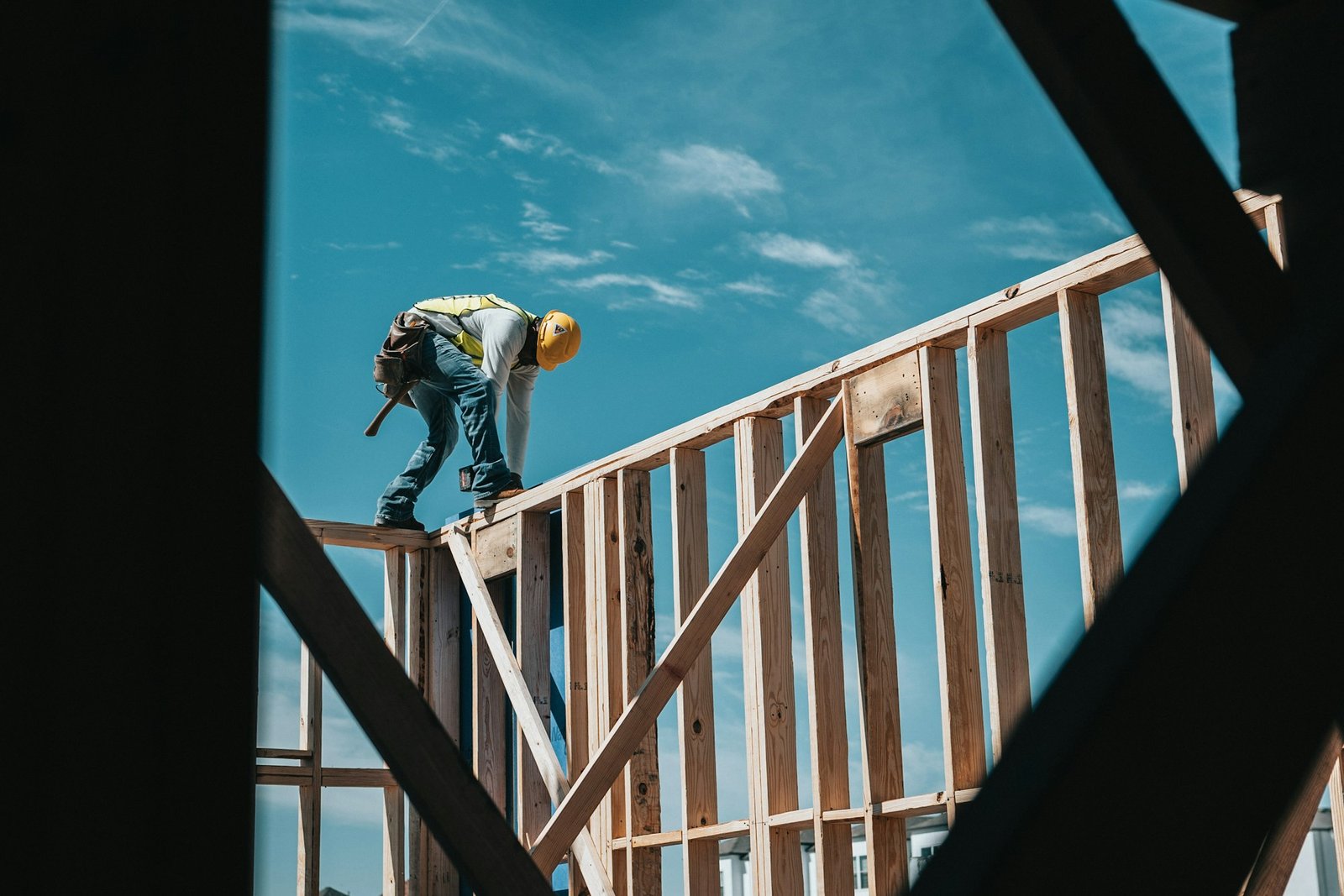Framer working high on a wood-frame residential build against a bright blue sky.
